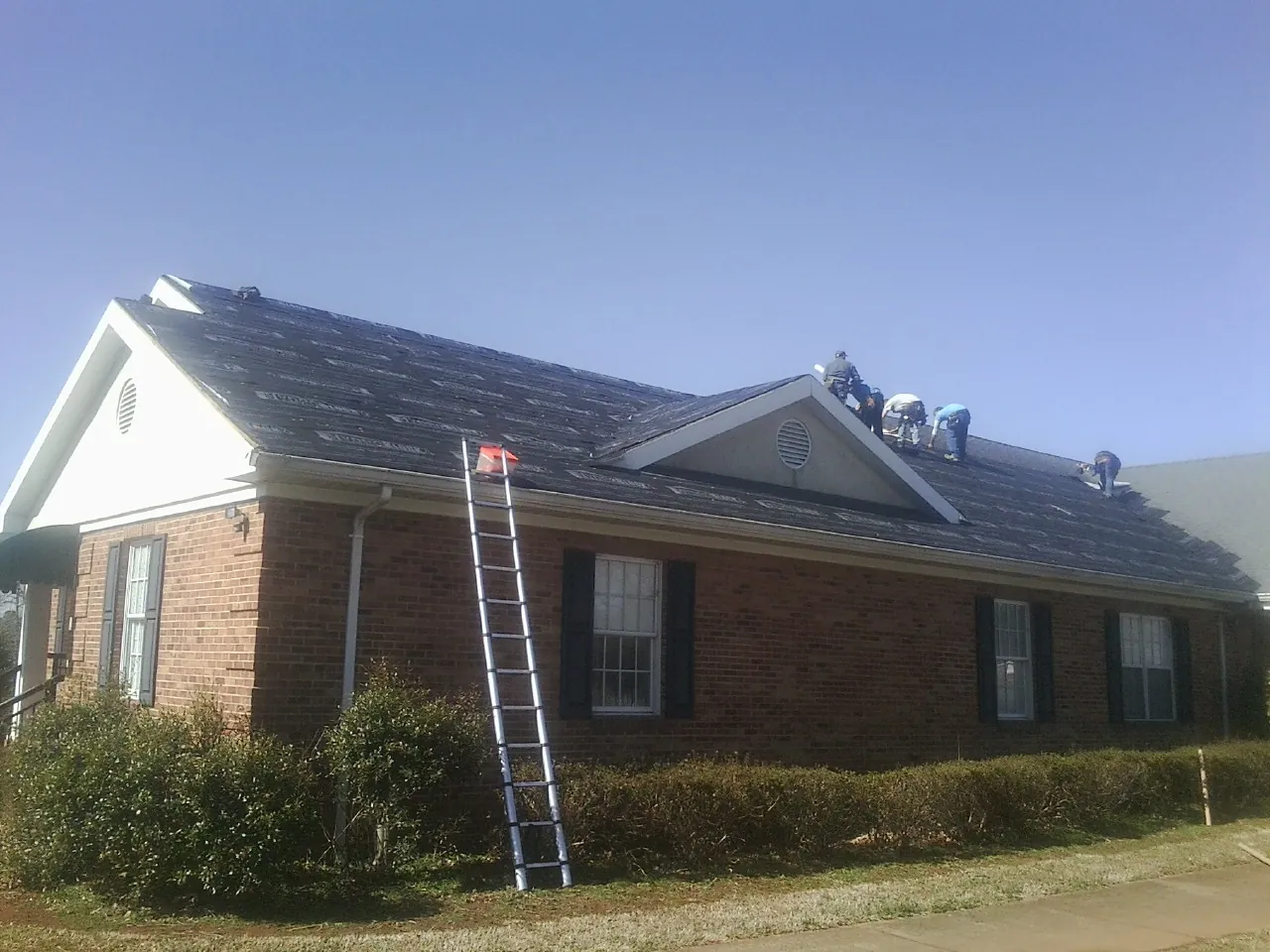 Crew tearing shingles off a brick ranch roof with a ladder set — Metal Roof Repair work by our crew in Mount Olive
