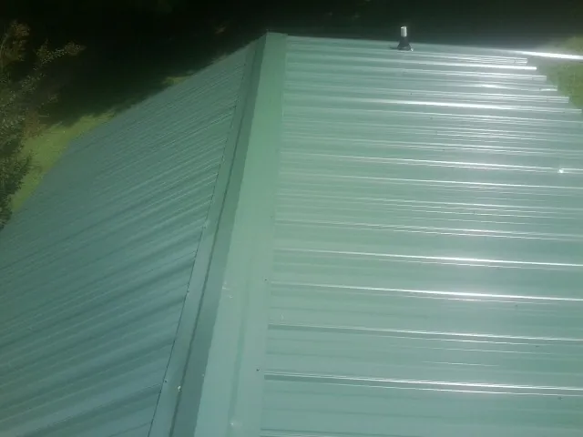 New green metal panels meeting at the ridge of a roof — Flat Roof Repair work by our crew in Mount Olive