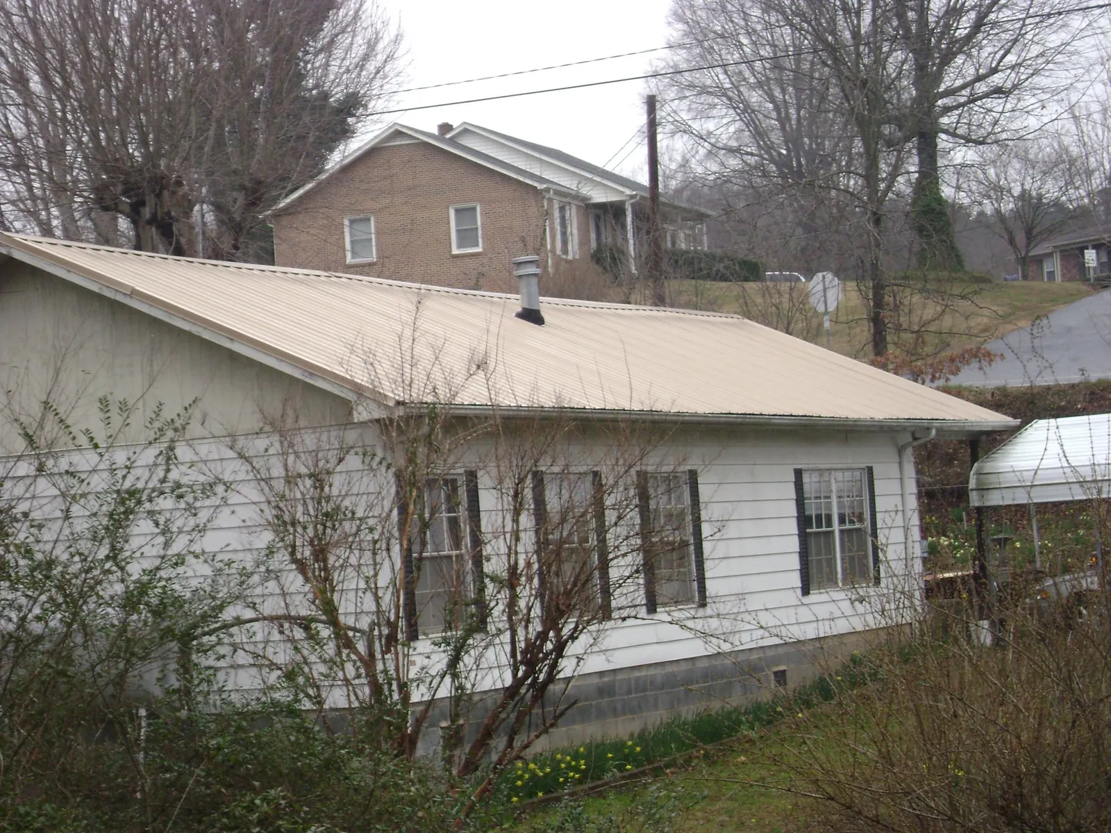 Tan metal roof on a white sided house set into a hillside — Commercial Roofing by Roofing Brothers in Mount Olive