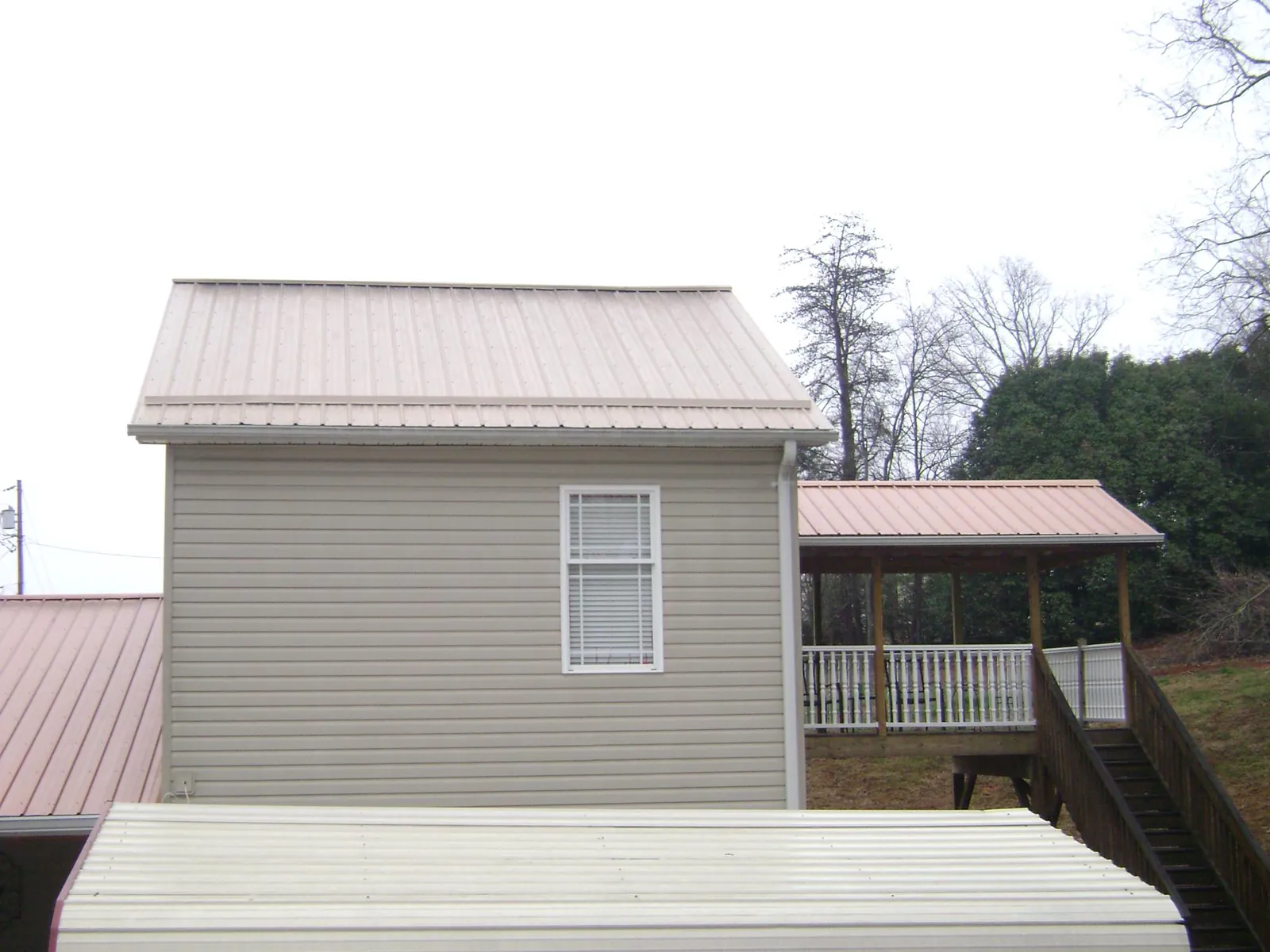 Tan metal roofs on a two story addition and attached porch, from a Roof Replacement job in Mount Olive